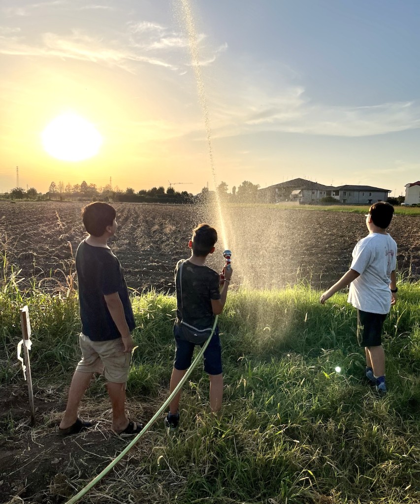 Tre ragazzi in un campo al tramonto, uno irriga con la canna dell'acqua